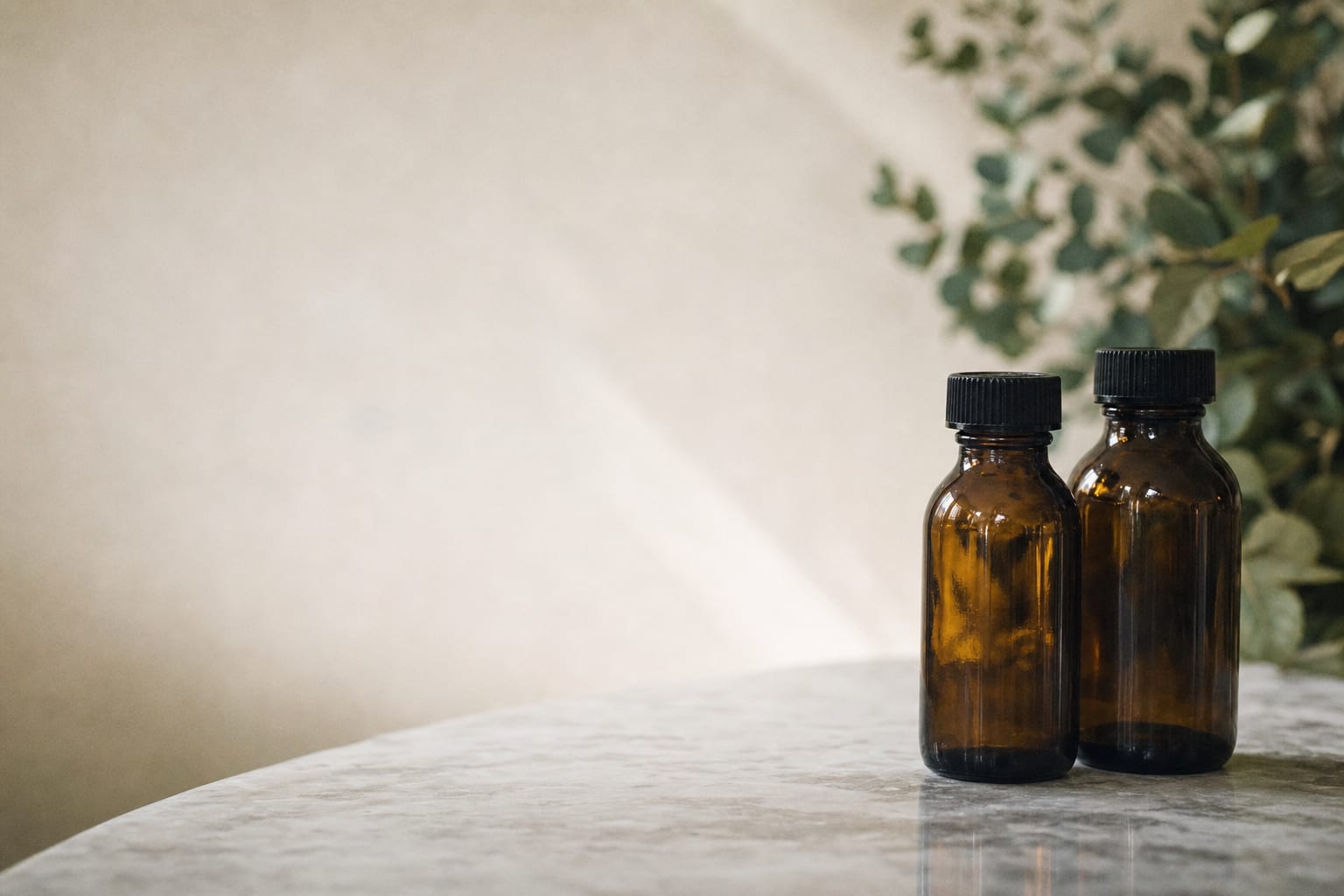 Plain amber bottles with black caps and a sprig of greenery in soft natural light